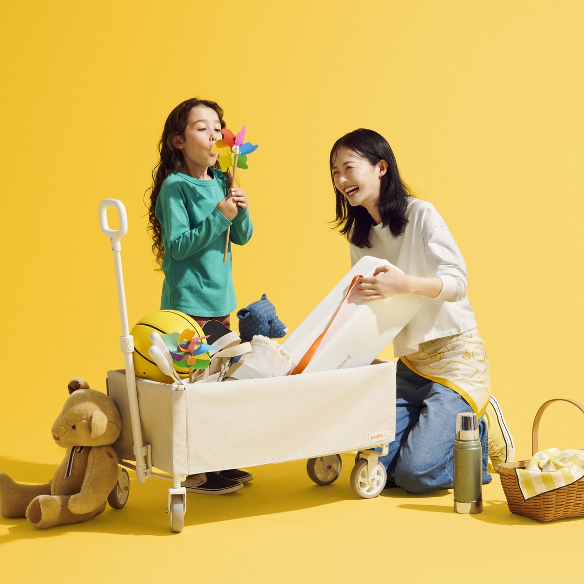 yocabitoのおしゃれな白のキャリーワゴンでピクニックを楽しむ母と娘。風車やランチボックスを持った、笑顔あふれるアウトドアのイメージ