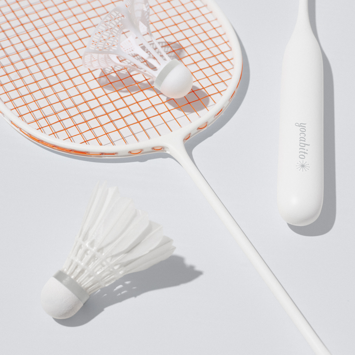 白を基調としたシンプルなyocabitoのバドミントンラケットVALENCIA。グリップのロゴとオレンジのガットがおしゃれなデザイン。